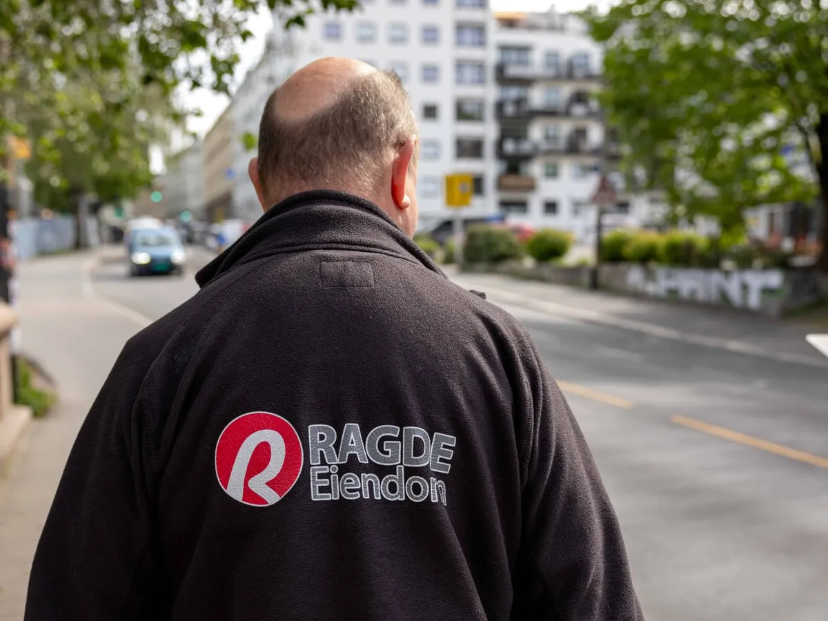 Guttorm Normann fra Ragde Eiendom på vei bortover gaten, sett bakfra i arbeidsjakken