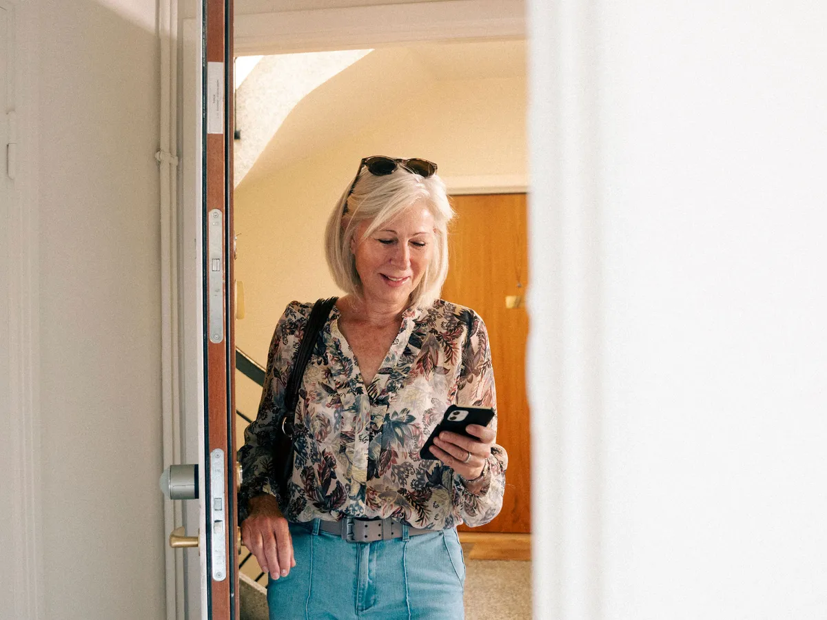 En kvinne går ut den åpne døren, med mobilen i hånden